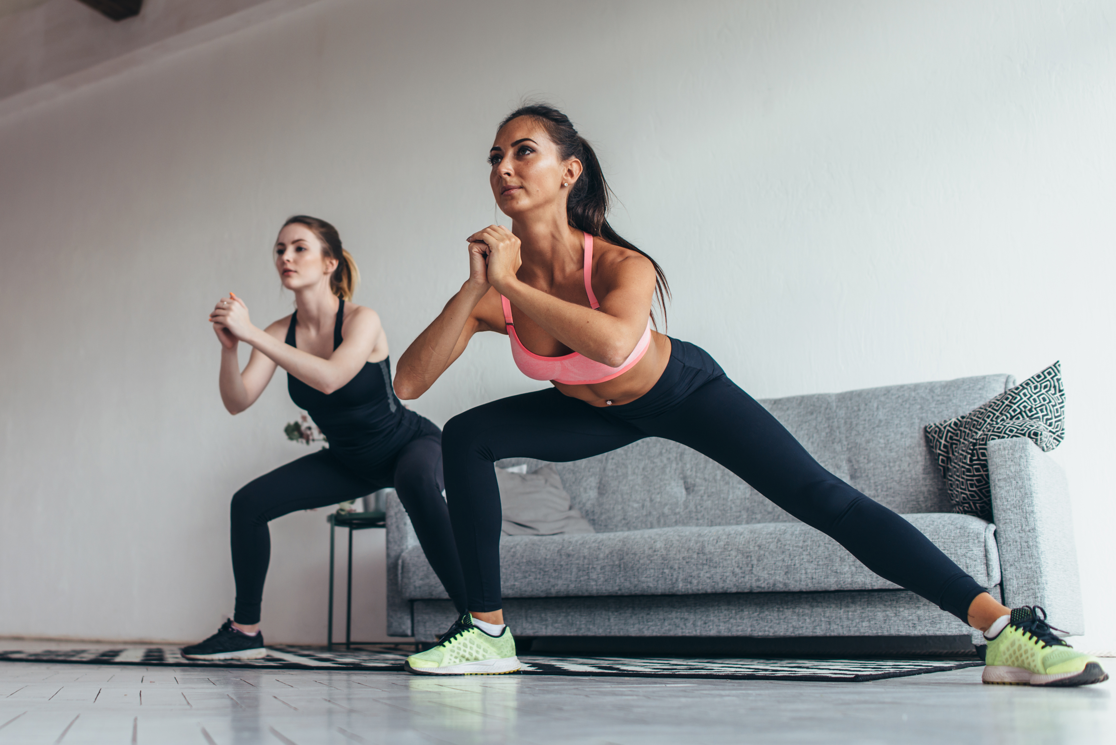 Two fit girls doing home workout performing lateral lunges at home.